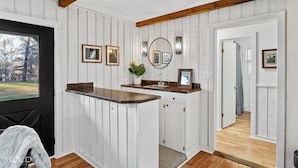 Una cocina con encimera de madera, armarios blancos y vistas a través de una ventana.