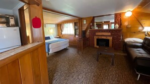 Una habitación acogedora de estilo cabaña con una cama, una pequeña mesa, una chimenea y un sofá.