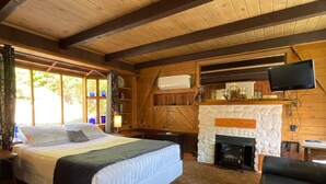 Una habitación de cabaña de madera con una cama, una chimenea, un televisor y un sillón de cuero.