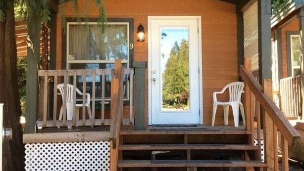 Una cabaña con fachada de madera, un porche delantero con dos sillas y una escalera que lleva a la entrada.