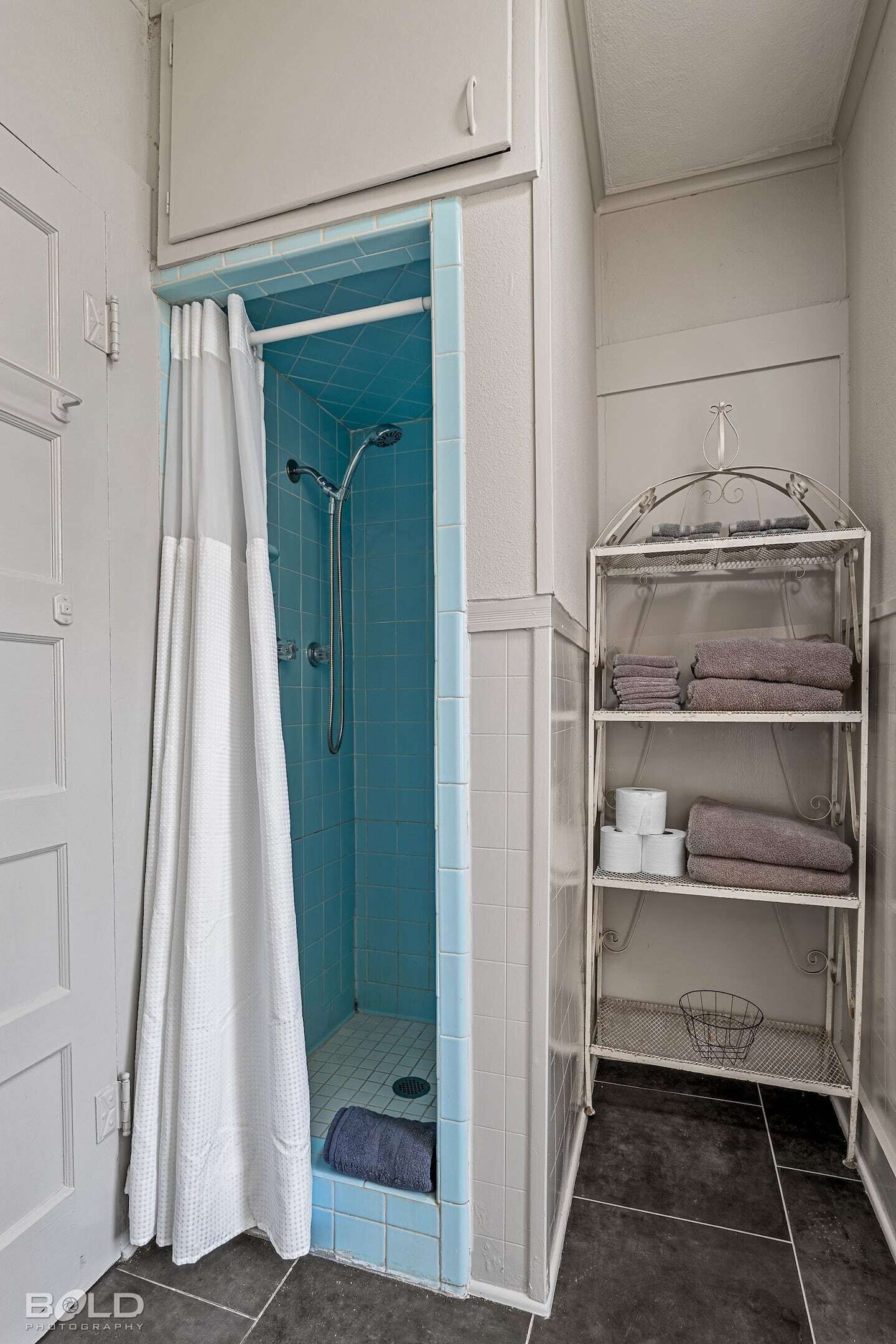 A bathroom with a shower, a towel rack, and a shelf with towels and toiletries.