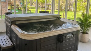 Ein Whirlpool in einem überdachten Außenbereich mit großen Fenstern, einem Deckenventilator und Blick auf einen Garten.