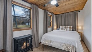 Une chambre à coucher avec un lit, un ventilateur de plafond en bois, une cheminée et une fenêtre avec des rideaux.