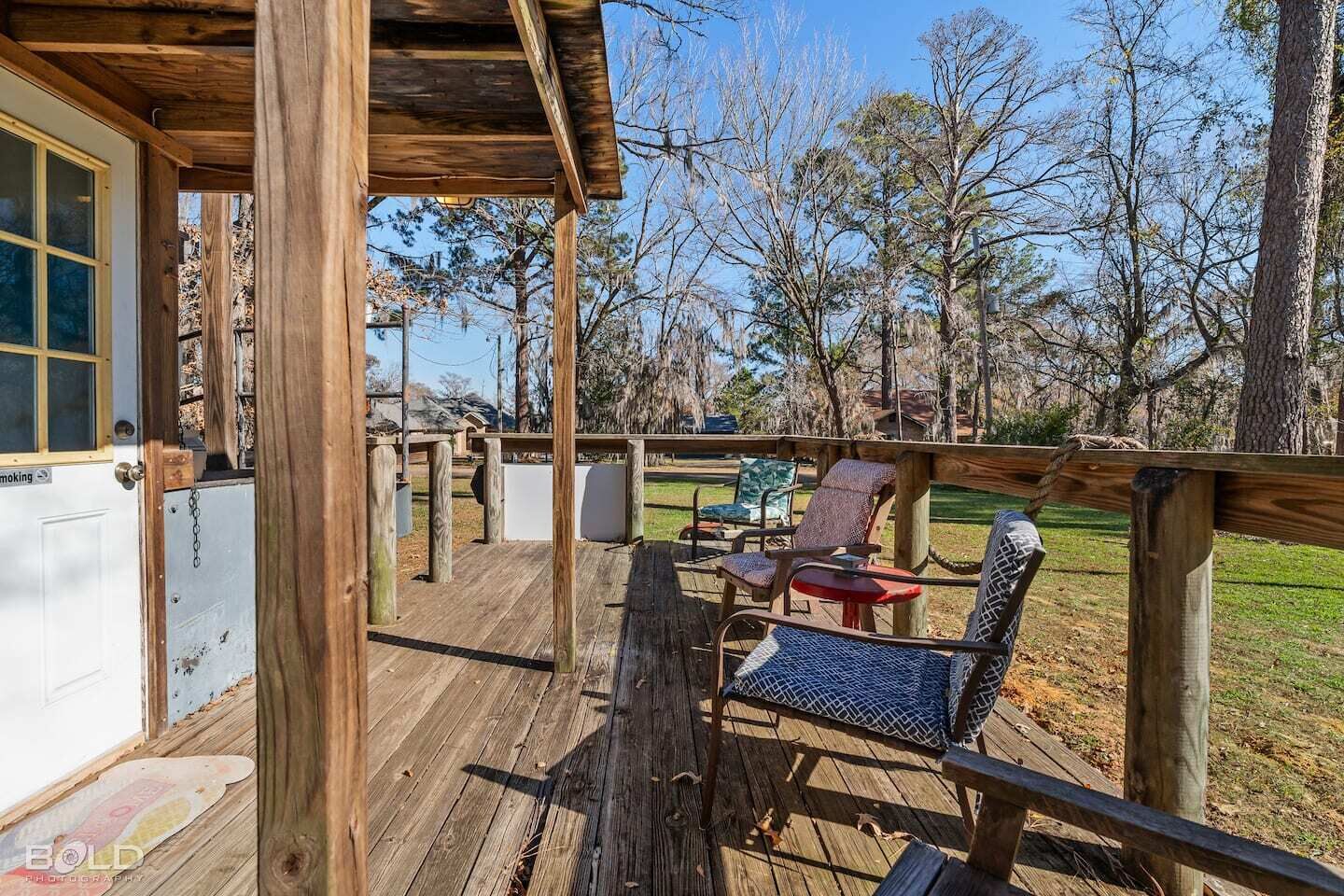 Una terraza de madera con asientos exteriores, una zona cubierta y vistas a los árboles circundantes.