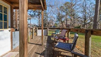 Una terraza de madera con asientos exteriores, una zona cubierta y vistas a los árboles circundantes.