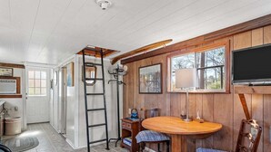 A cozy room with a wooden dining table, two chairs, a ladder, and a television mounted on the wall. - Unforgettable Experience: Enjoy a maritime adventure unlike any other. Unwind in a cozy little ship with upper and lower decks with private dock access (Karnack)