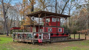 A red lodge with a covered deck and a sign reading 'Hodge Podge Cottages.' - Unforgettable Experience: Enjoy a maritime adventure unlike any other. Unwind in a cozy little ship with upper and lower decks with private dock access (Karnack)