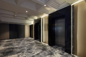 Un pasillo con alfombra estampada, pared de mármol y un ascensor moderno.