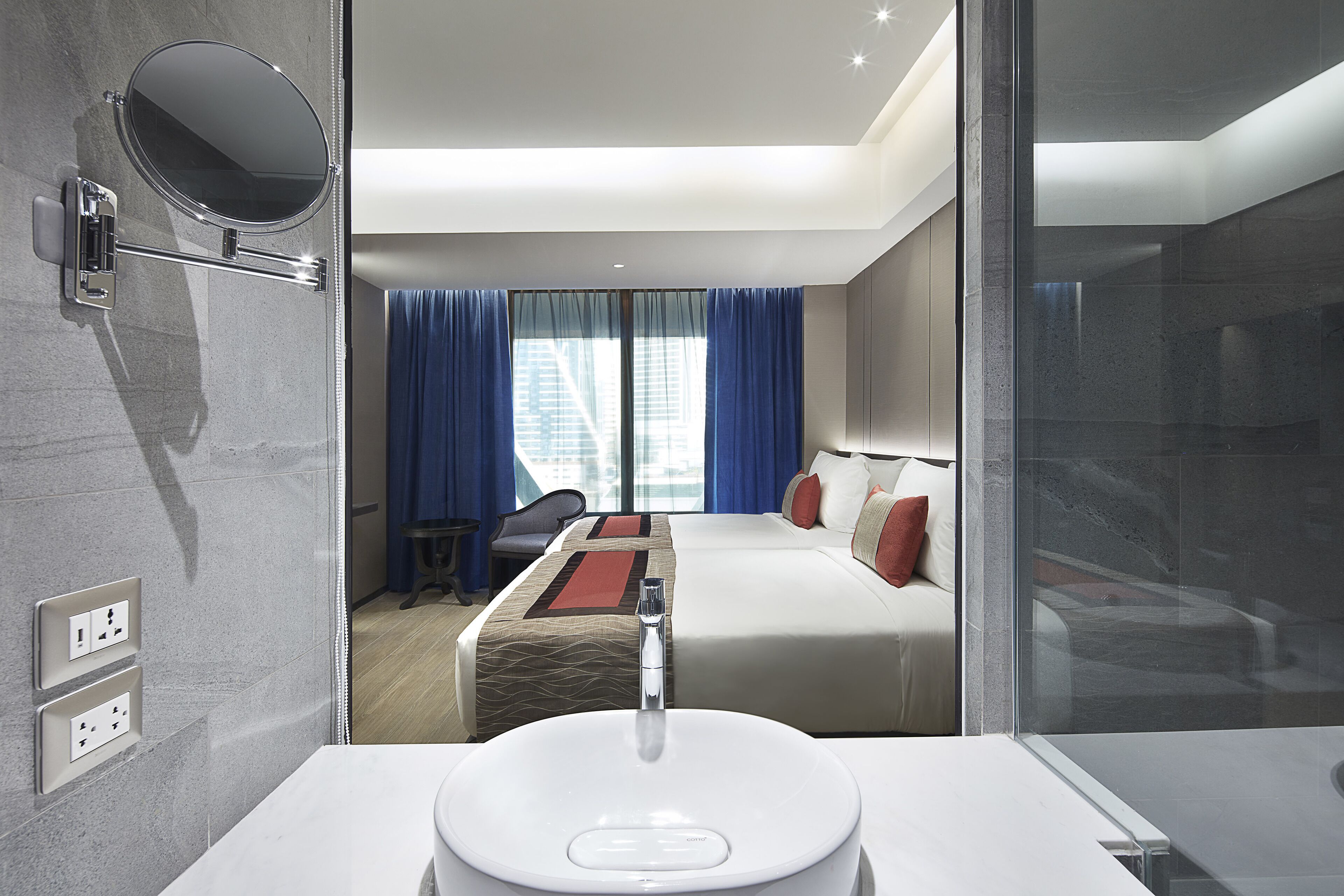 Ein modernes Hotelzimmer mit einem großen Bett, einem Schreibtisch und einem Badezimmer mit Waschbecken und Spiegel.