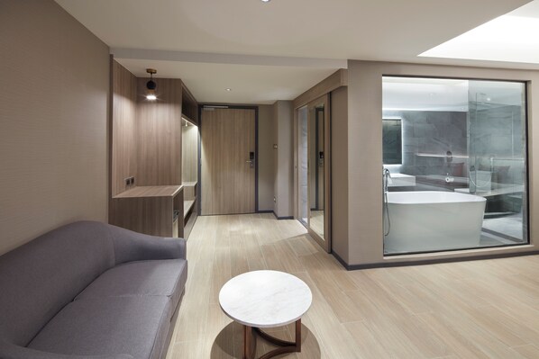 A modern hotel room with a sofa, a small round table, and a large glass shower area. - Grace At Five By Grace Hotel (Bangkok)