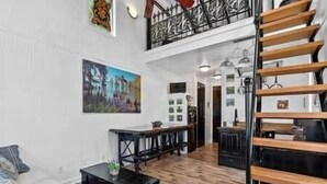 A spacious living area with a wooden staircase, a dining table, and a large painting on the wall. - Tiny Cajun Cabin (Breaux Bridge)