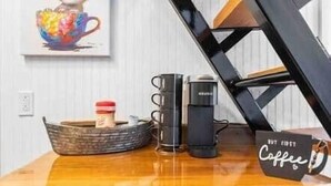 A wooden table with a coffee maker, a mug, and a sign that reads "Buy First Coffee." - Tiny Cajun Cabin (Breaux Bridge)