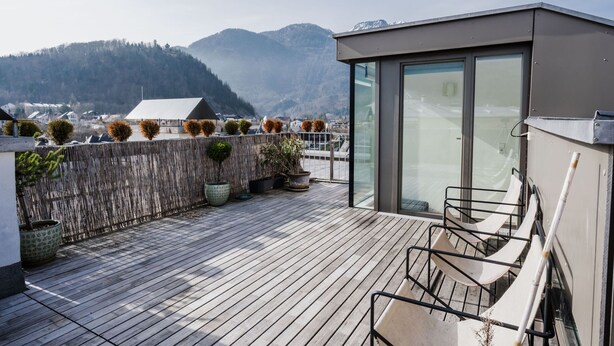 Une terrasse sur le toit, dotée d’une plateforme en bois, de plantes en pot et d’un espace clos par des parois de verre.