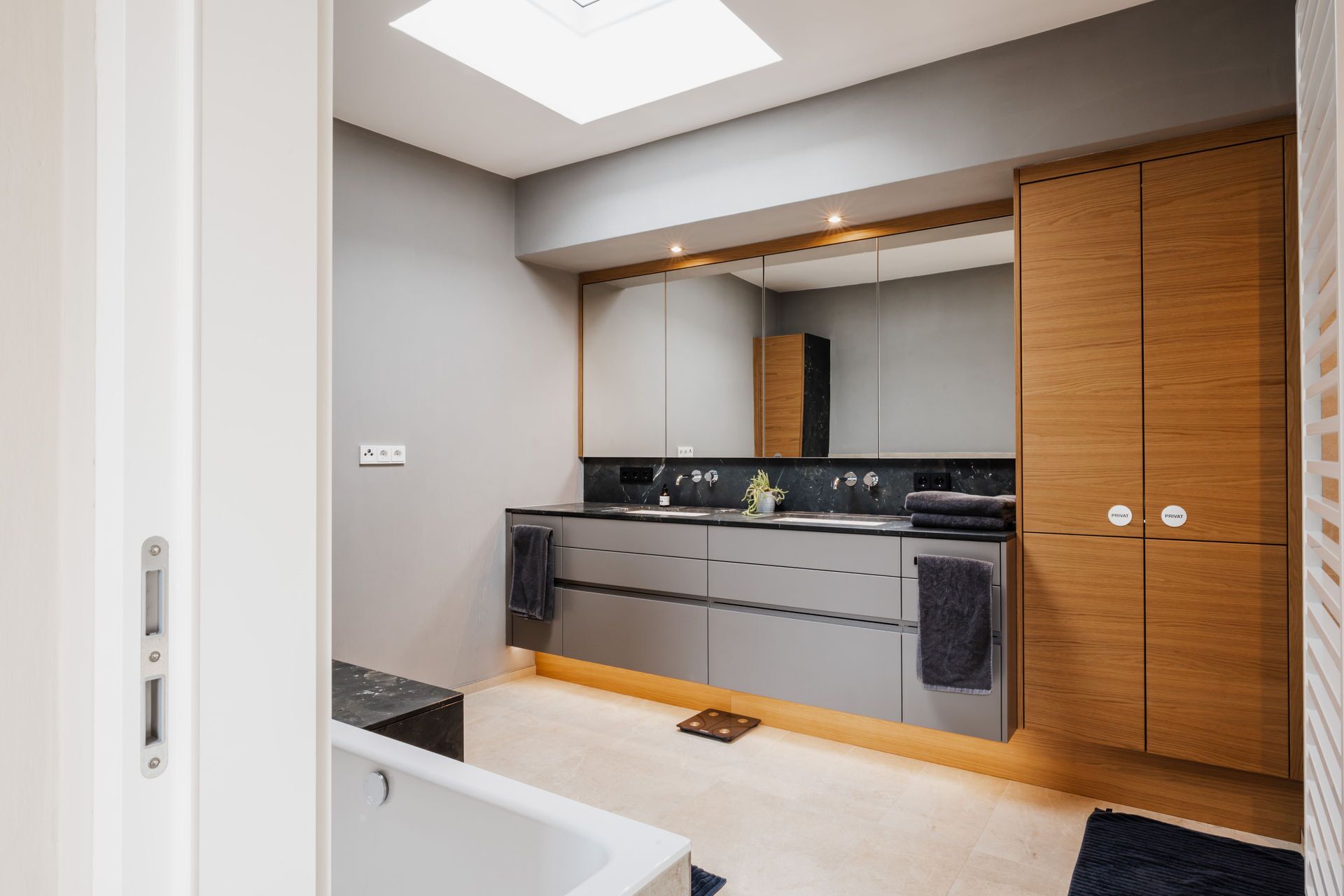 Un baño moderno con un espejo grande, una bañera y armarios de madera.