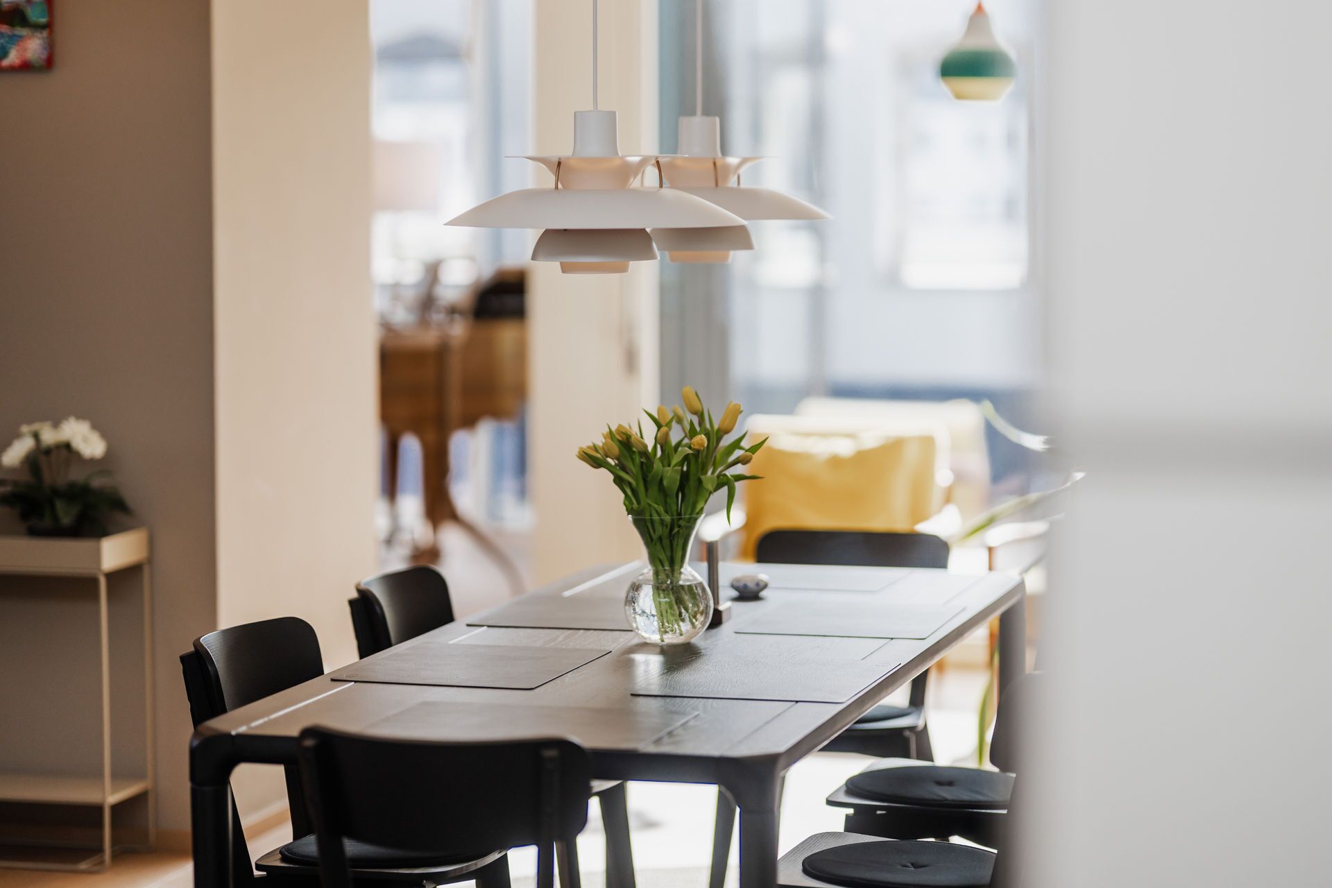Un'area pranzo moderna con un tavolo lungo, sedie nere e un vaso di fiori gialli.
