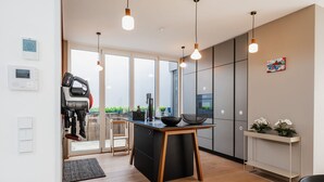 Une cuisine moderne dotée d’un îlot central, de luminaires suspendus et offrant une vue sur l’extérieur.