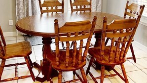 A dining room with a round wooden table and six chairs, a chandelier, and a view of the outdoors through a window with curtains. - Rogers Retreat, Dog Friendly, Cozy Home. Close to Walmart Amp, Downtown Rogers (Rogers)