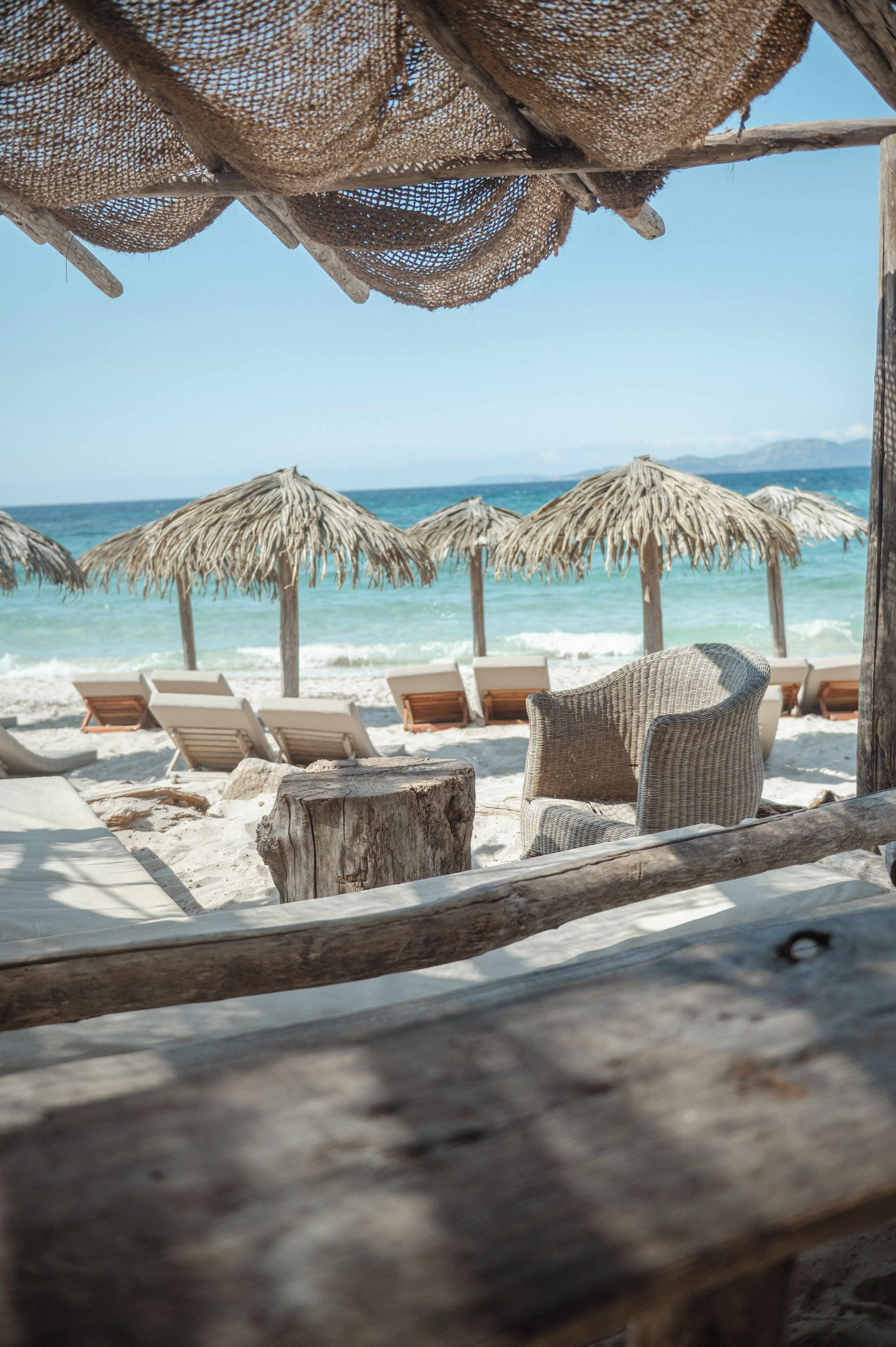 Una playa con sombrillas de paja y sillas de mimbre.