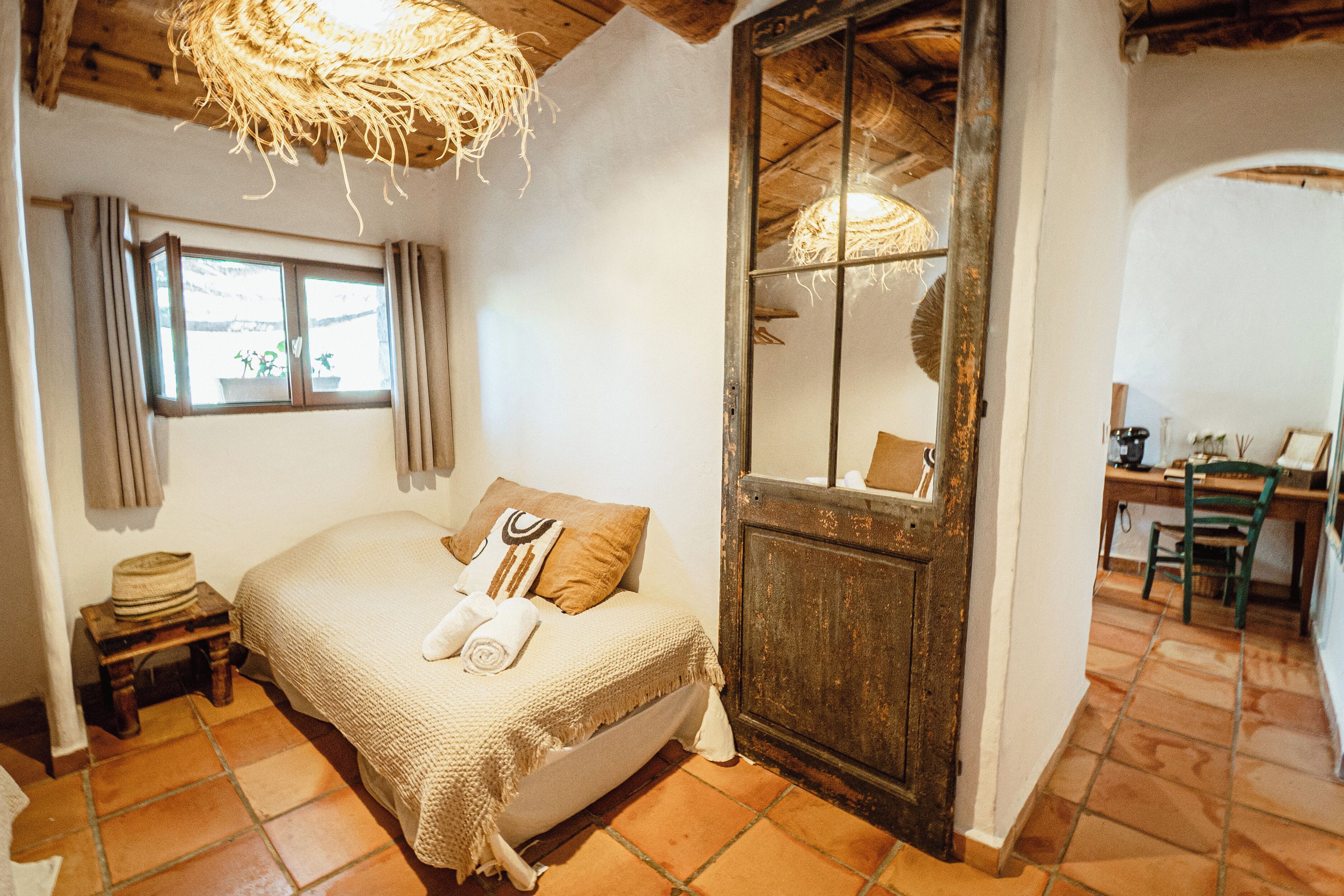 Un dormitorio acogedor con una cama, una mesita, una ventana con cortinas y una puerta rústica.