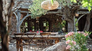 Un espace de restauration en plein air avec des murs en pierre, des tables et des chaises en bois, et une jardinière suspendue.