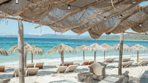 Une plage avec des parasols en chaume et des chaises longues en bois, tous orientés vers la mer.