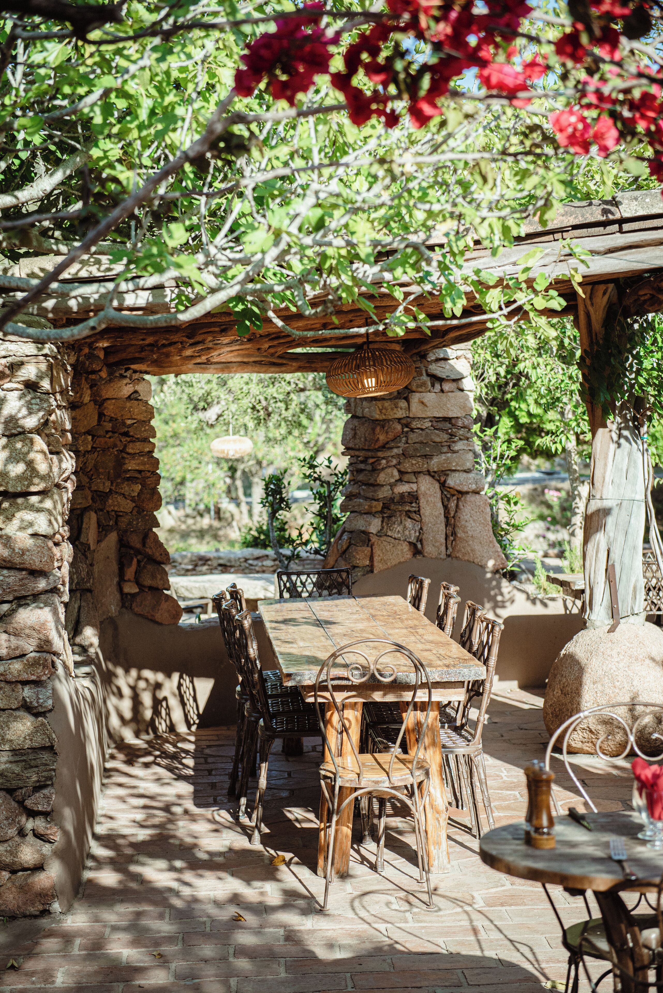 An outdoor patio with stone walls, wooden furniture, and a hanging light fixture.