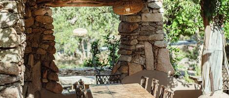 An outdoor patio with stone walls, wooden furniture, and a hanging light fixture.