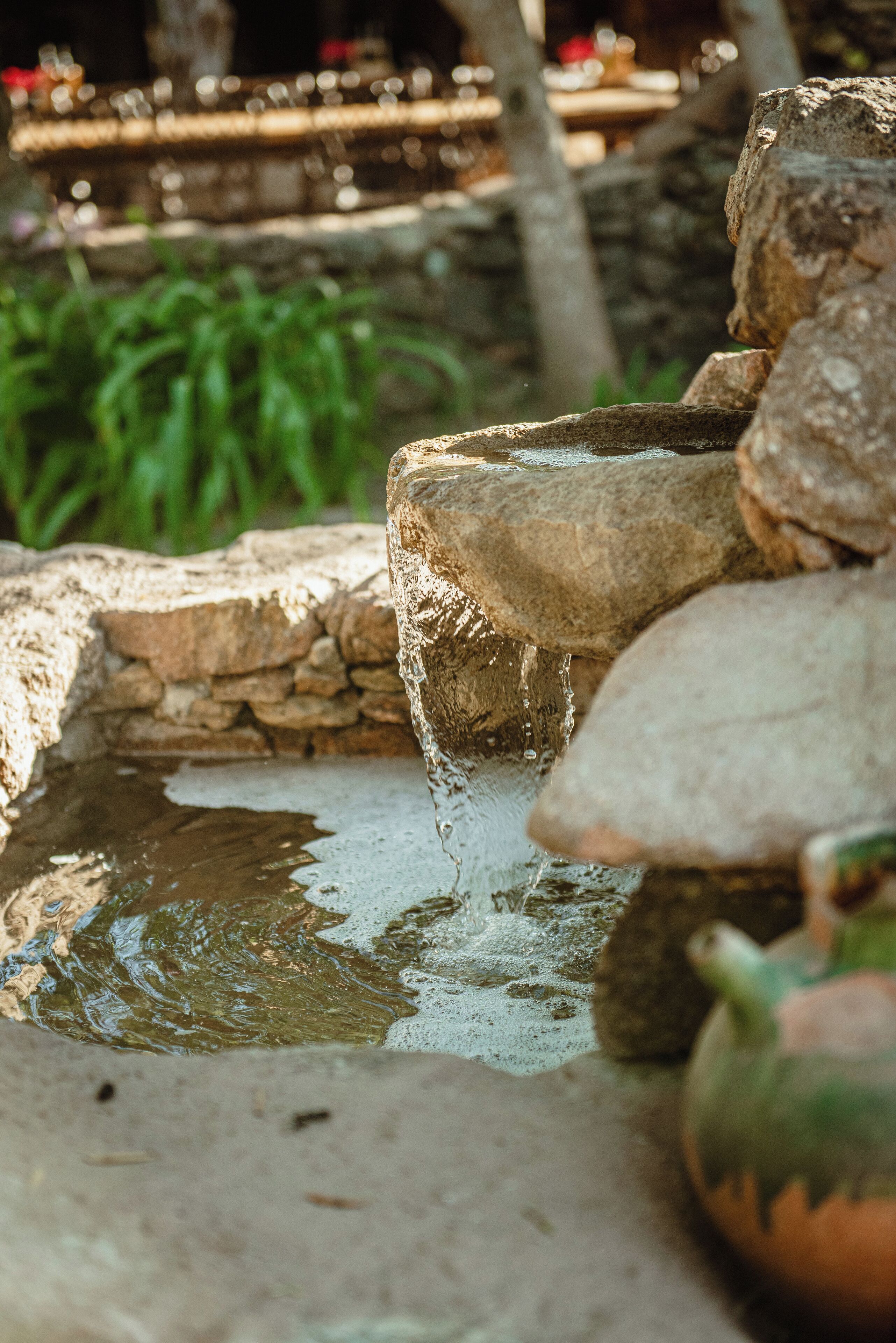 A stone water feature with a small stream flowing over rocks, surrounded by greenery.