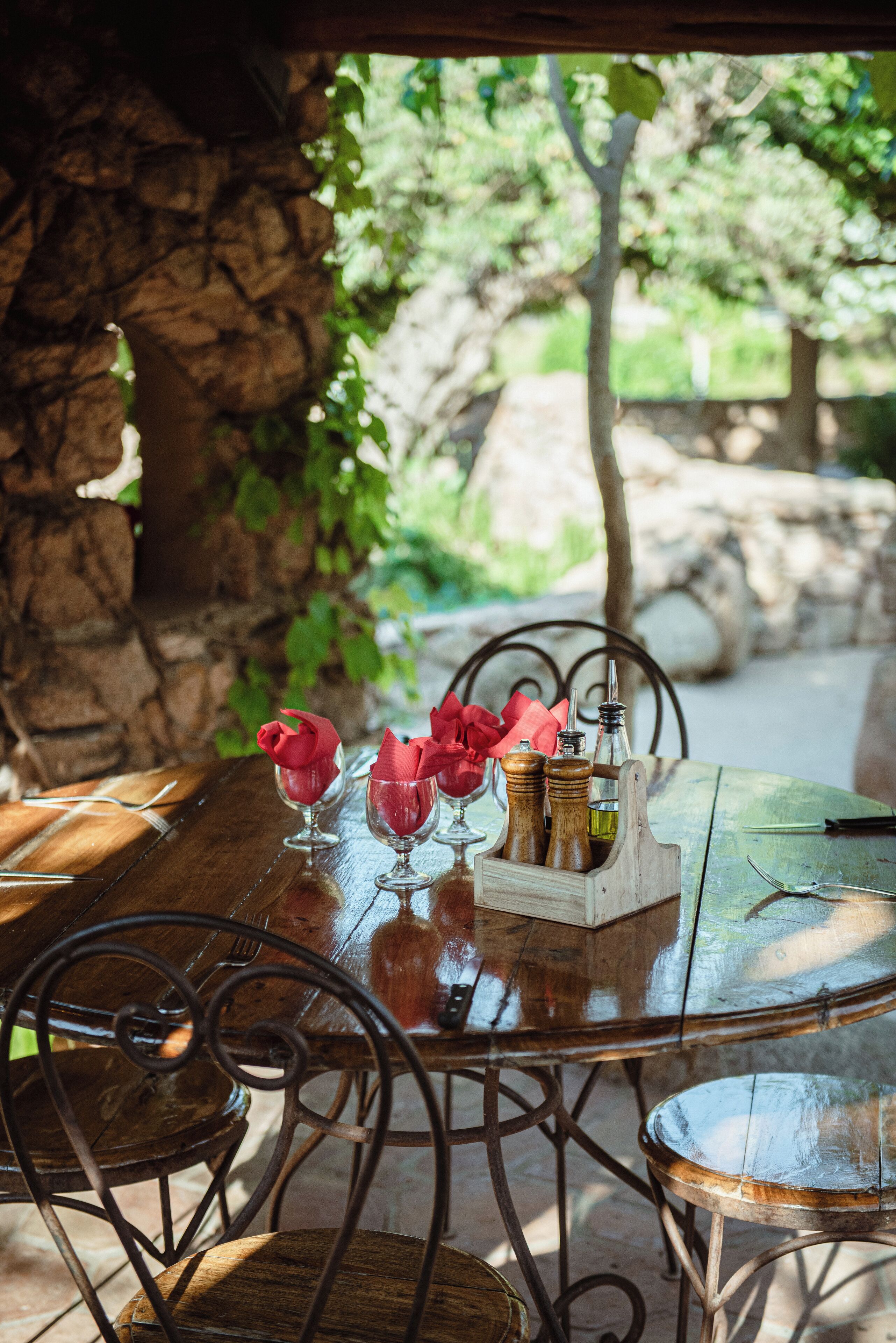A wooden table with metal chairs, a glass vase with red flowers, and a wooden salt and pepper shaker set.