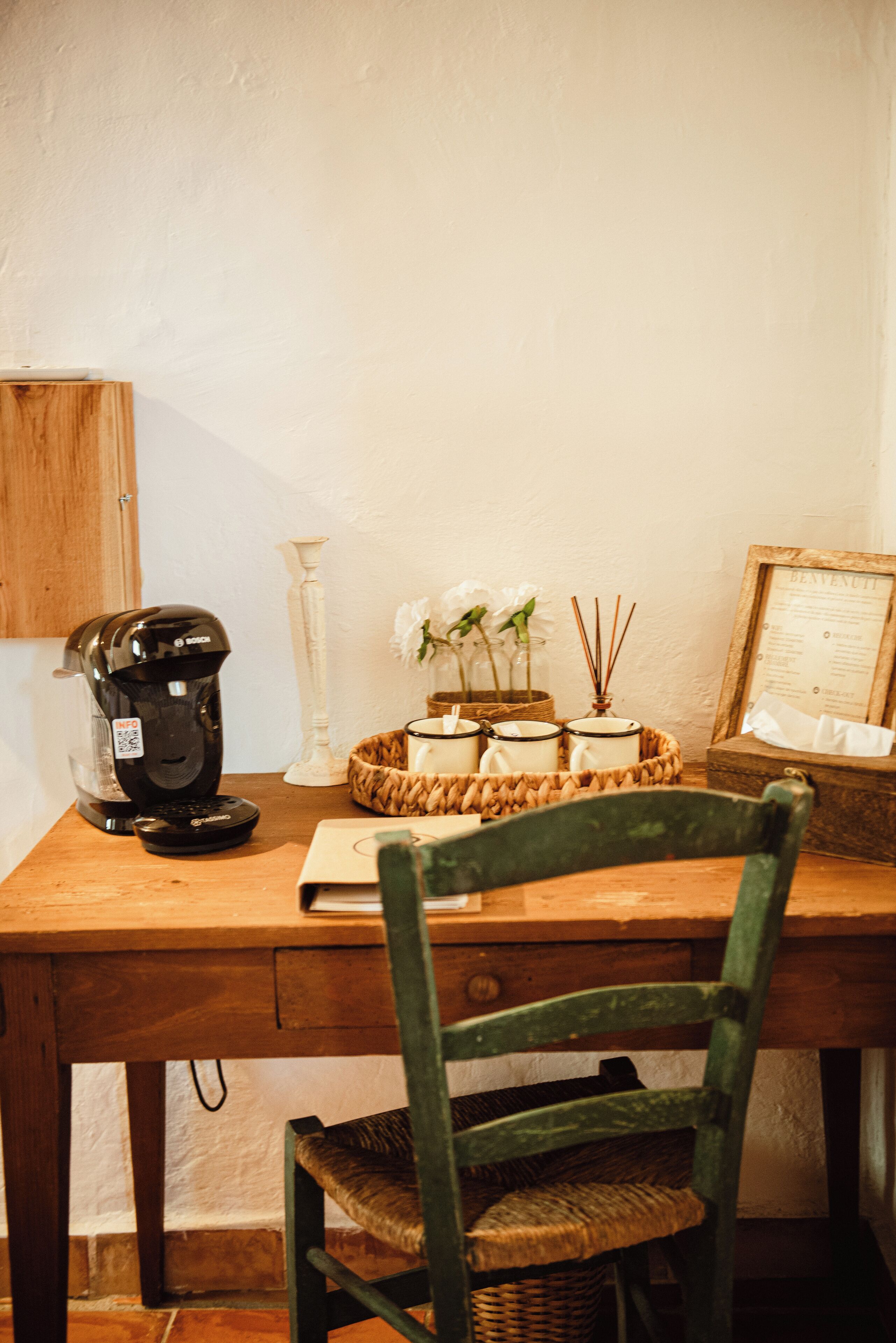 A wooden desk with a coffee maker, a basket with candles, and a framed menu.