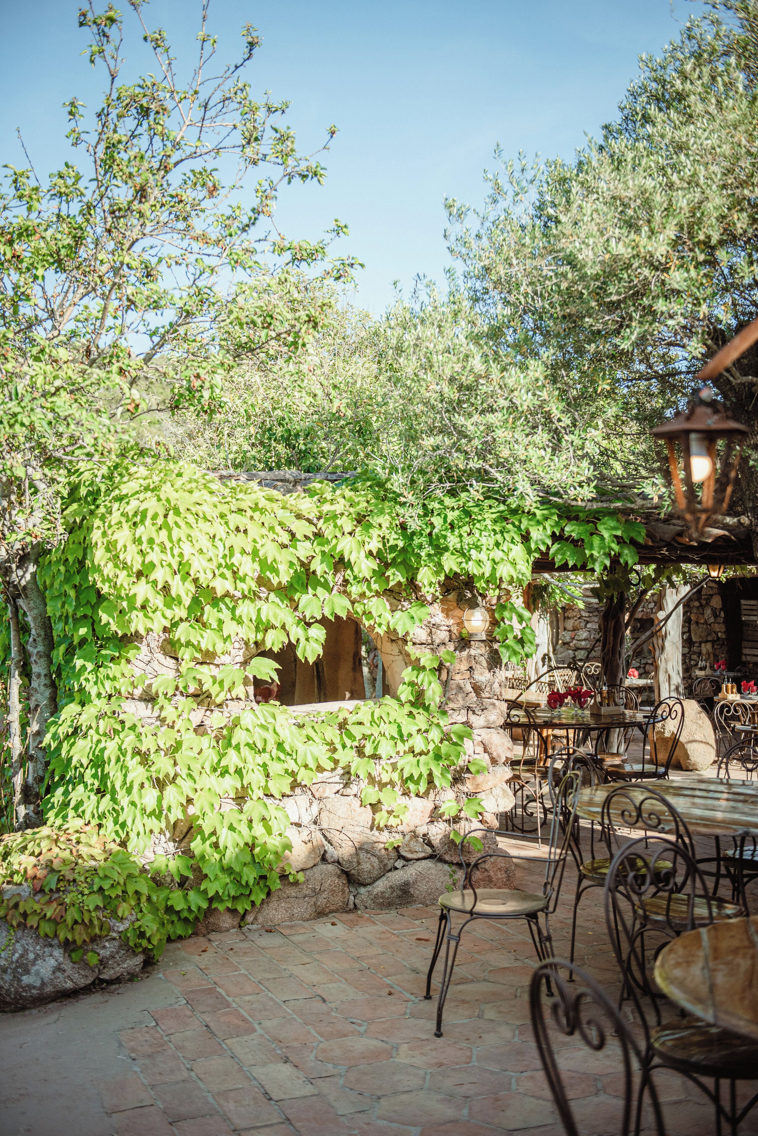 Une terrasse extérieure avec des murs en pierre, une arche en pierre et des meubles en métal.