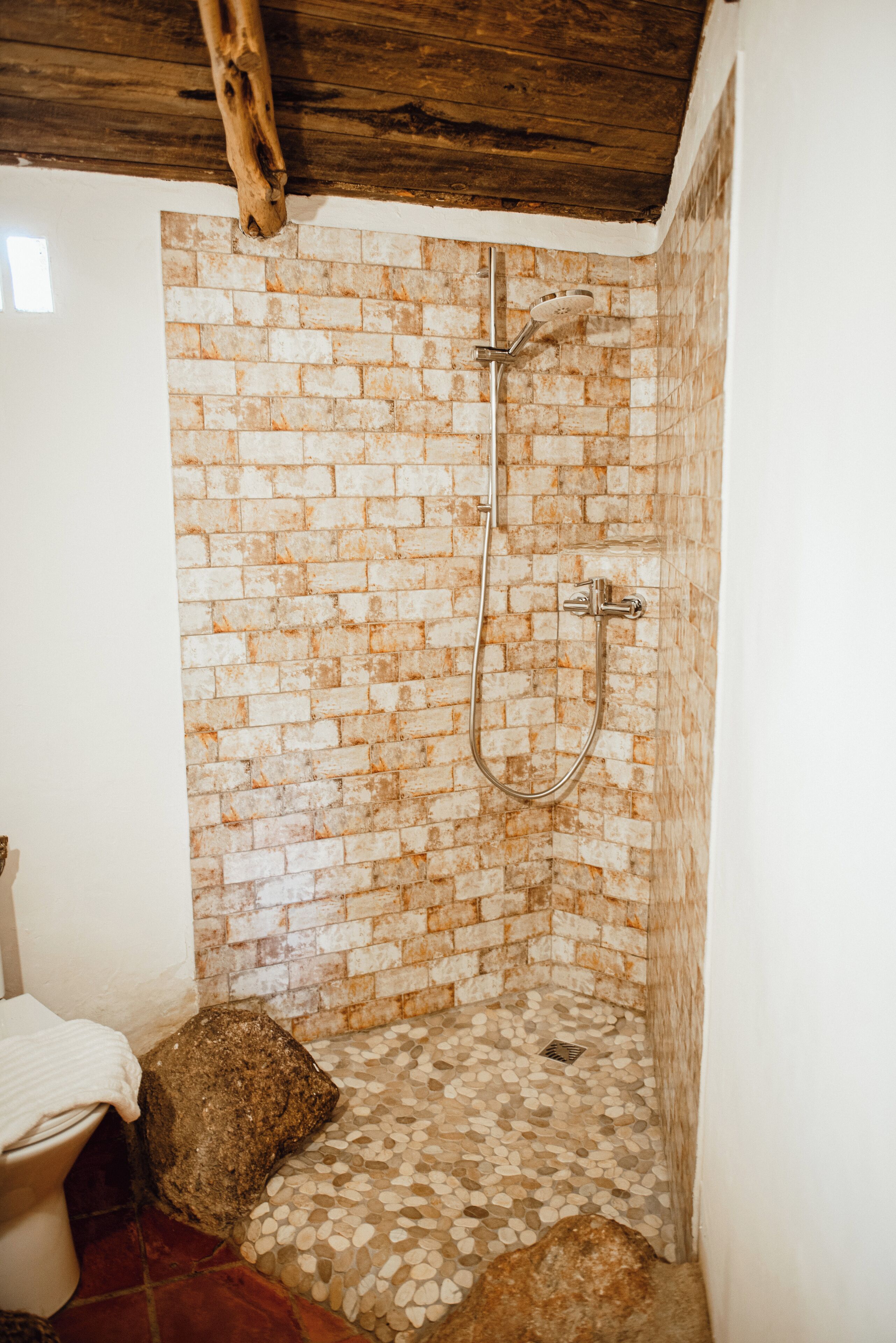 Une douche avec un mur en briques et un plafond en bois.