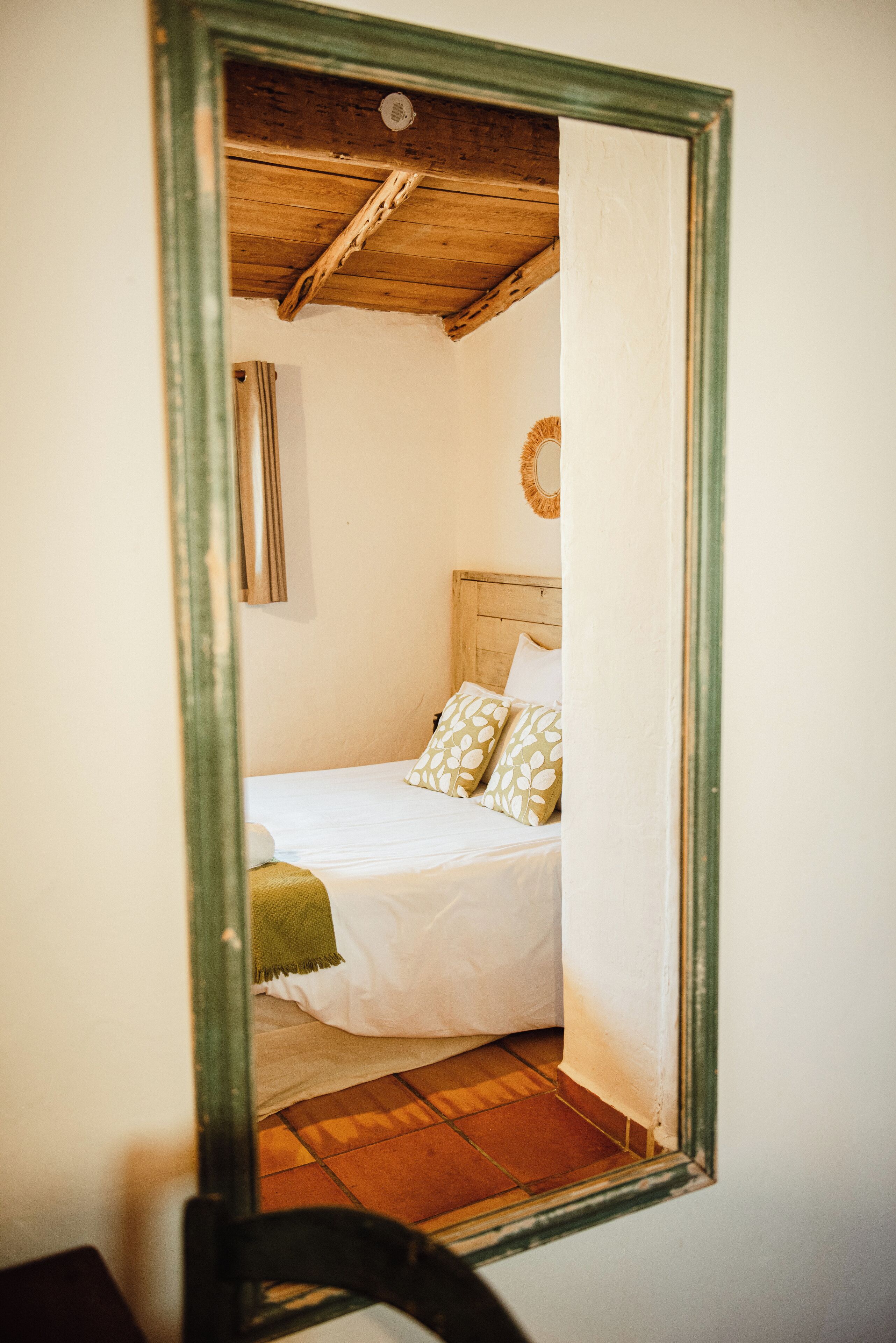A bedroom with a wooden ceiling, a bed with patterned pillows, and a mirror on the wall.