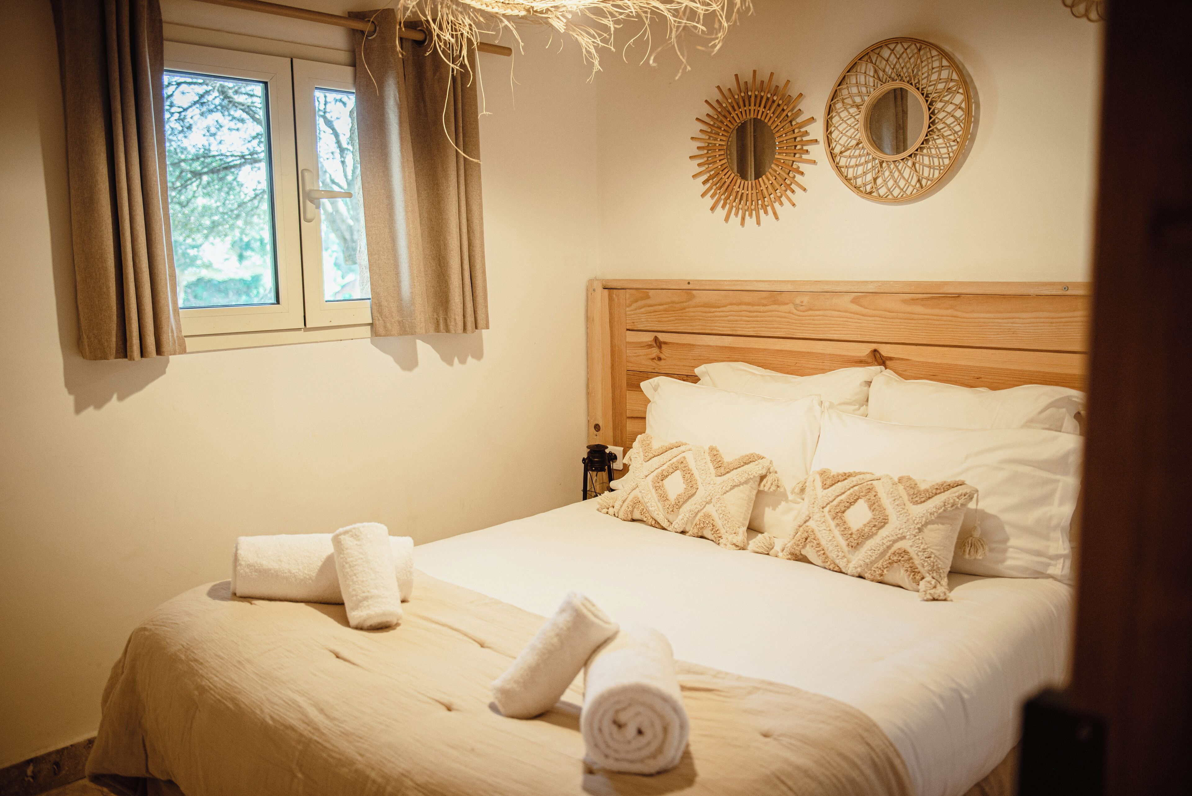 A neatly made bed with white linens and decorative pillows, a window with curtains, and two wall-mounted mirrors.