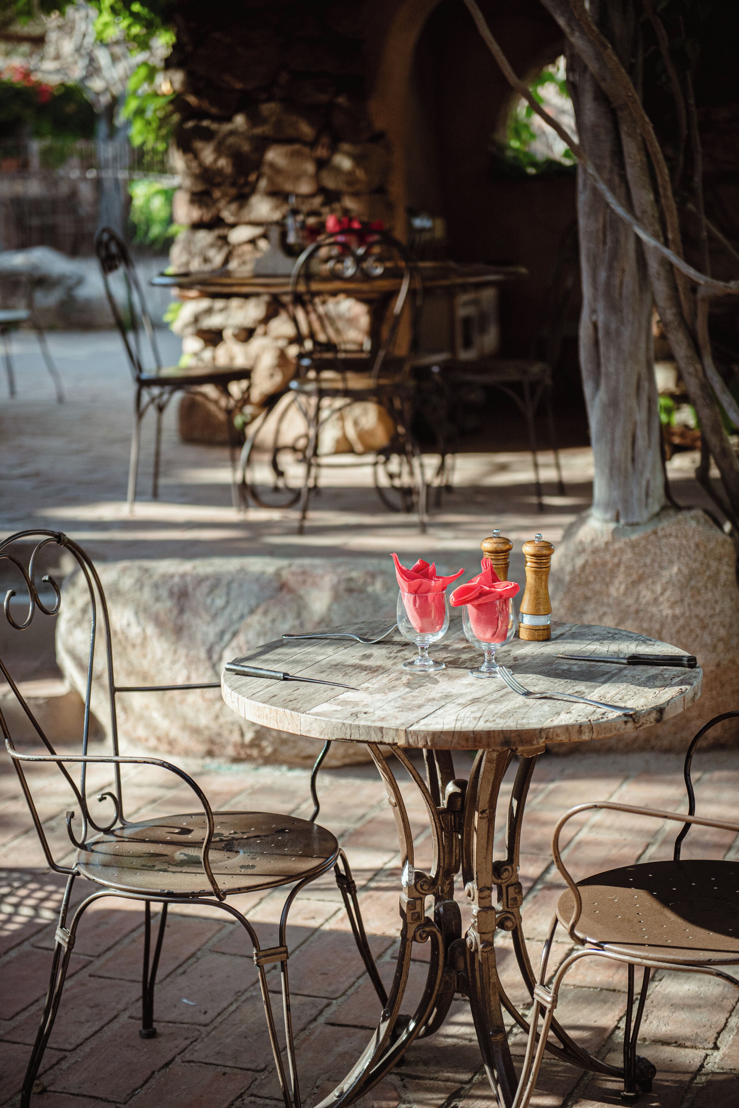 A round table with metal chairs, a stone wall, and a tree in the background.