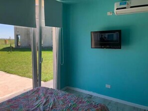 Relax in this serene room with a large window opening to a lush outdoor space, a flat-screen TV, and a comfortable bed with a vibrant bedspread.