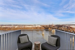 A balcony with two wicker chairs and a small table, overlooking a river and a bridge. - Eve Nashville (Nashville)