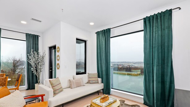 En moderne stue med sofa, stole, sofabord og et stort vindue med gardiner.