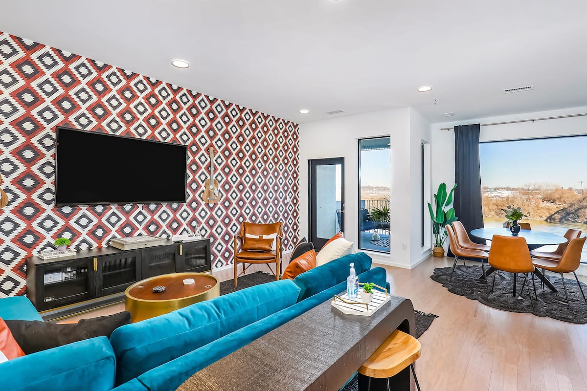 A modern living room with a large TV, blue sofas, a wooden coffee table, and a dining area with chairs and a table.