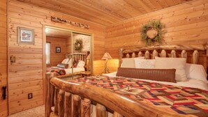 Een slaapkamer in een houten blokhut met een bed, nachtkastje, lamp en spiegel.
