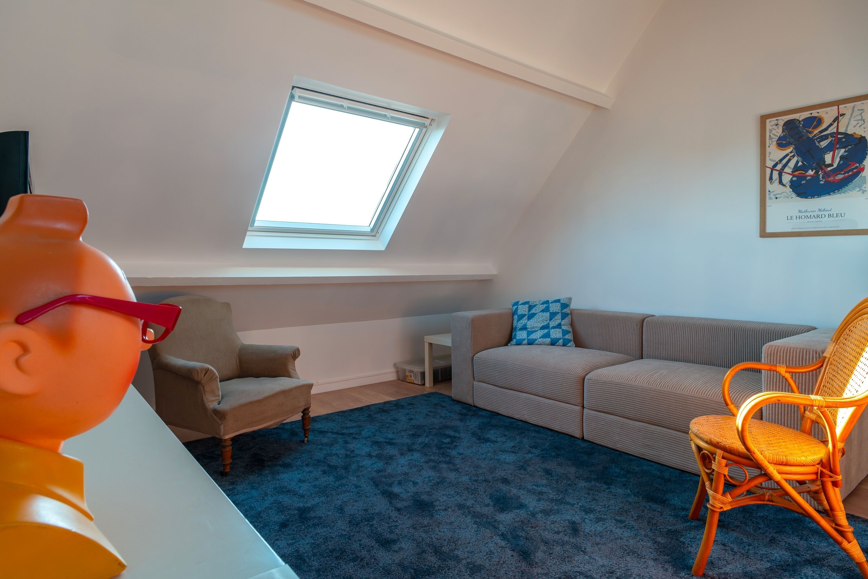 Een kamer met een schuine kap, dakraam, bank, stoel en tafel.