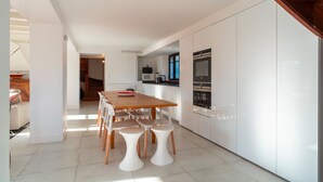 Una cocina moderna con armarios blancos, una mesa de comedor de madera y taburetes blancos.