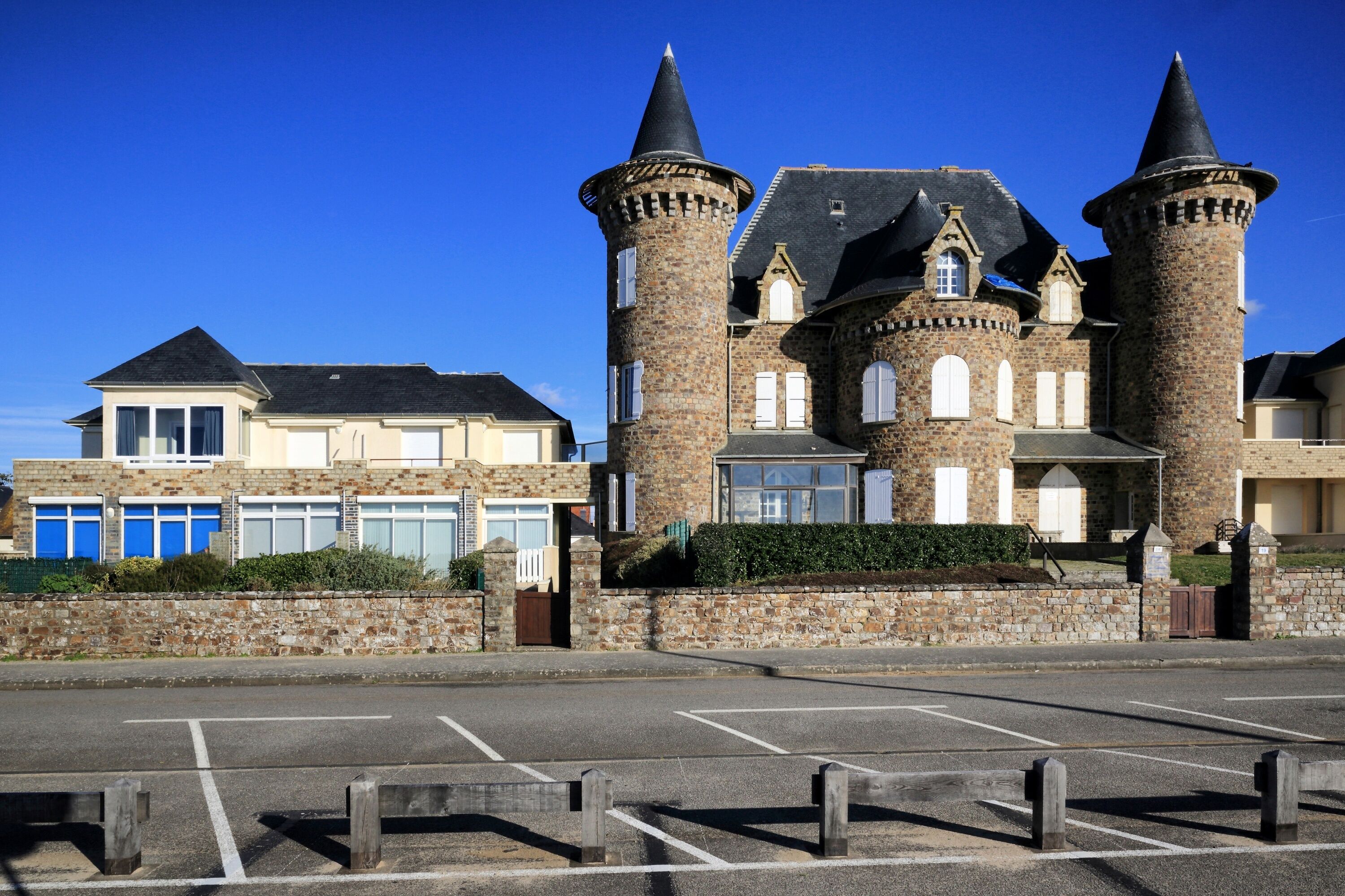 Un bâtiment qui ressemble à un château, avec deux tours imposantes, un parking et un ciel d’un bleu éclatant.