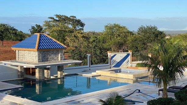 A swimming pool with a stone structure and a blue roof, surrounded by greenery and a view of the ocean. - Hacienda Teofila (Partido)