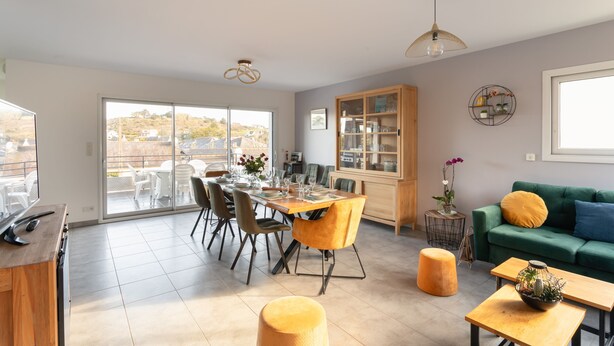 A spacious living area with a dining table set for six, a green sofa with a yellow pillow, and a wooden cabinet.
