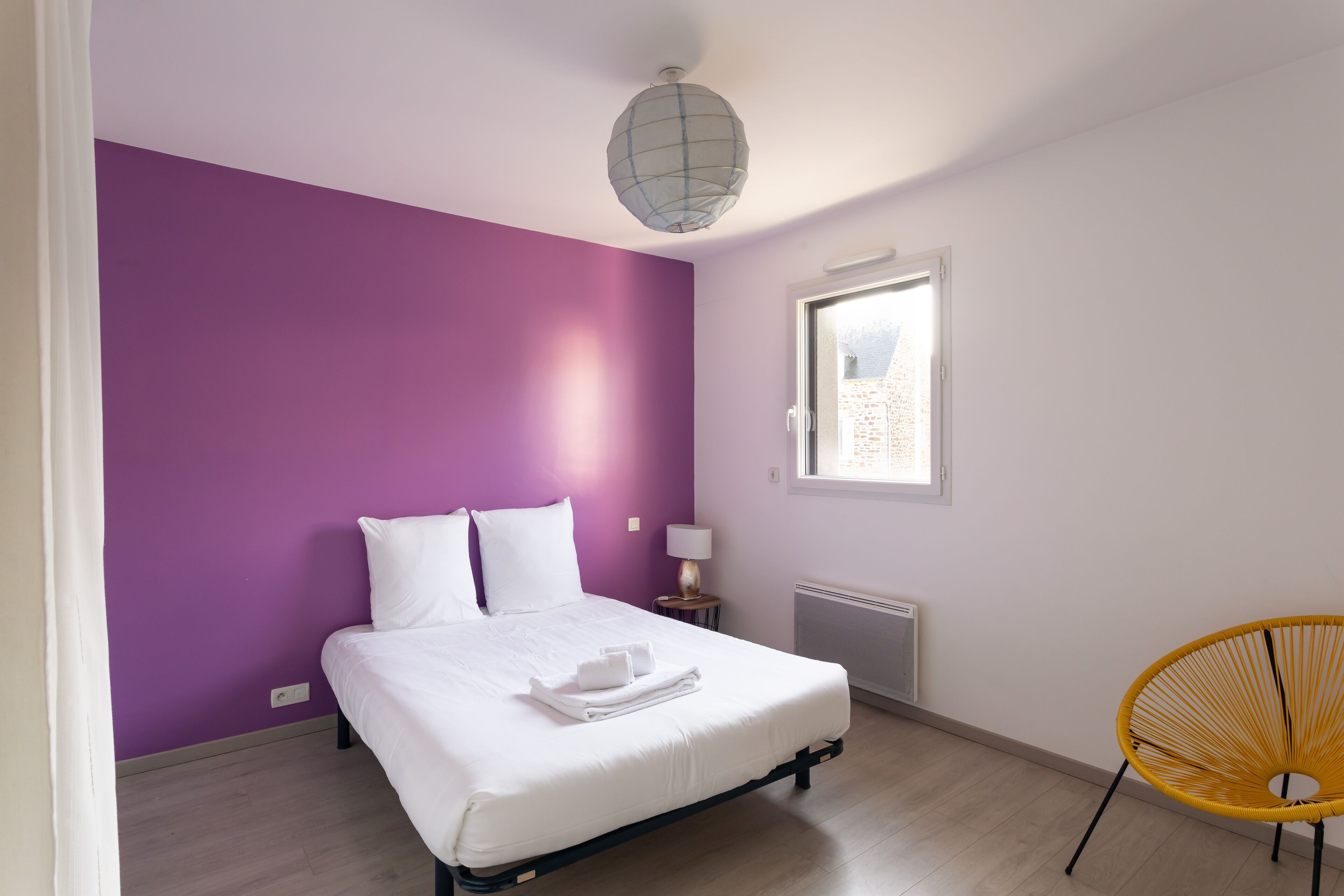 Un dormitorio con una cama, una ventana, una lámpara y una silla.