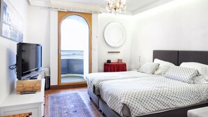 Un dormitorio con una cama, televisión, una mesita auxiliar roja, un espejo y vistas al exterior.
