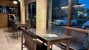 Et moderne spiseområde med træborde og stole, store vinduer med udsigt over bybilledet, og en stensøjle.