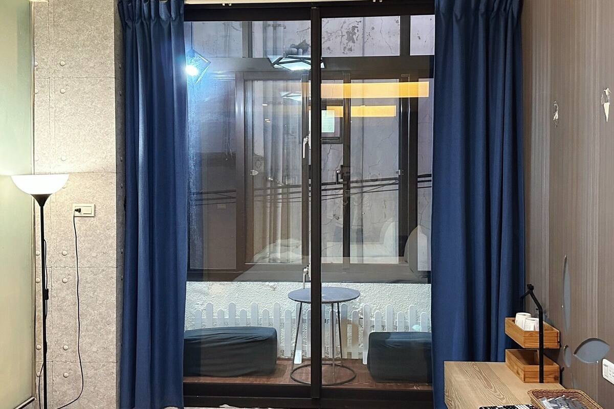 A room with a sliding glass door, a small round table, two chairs, a wooden bench, a lamp, and a shelf with items.