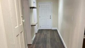 Un pasillo estrecho con suelo de madera y paredes blancas, que conduce a una puerta blanca al final.